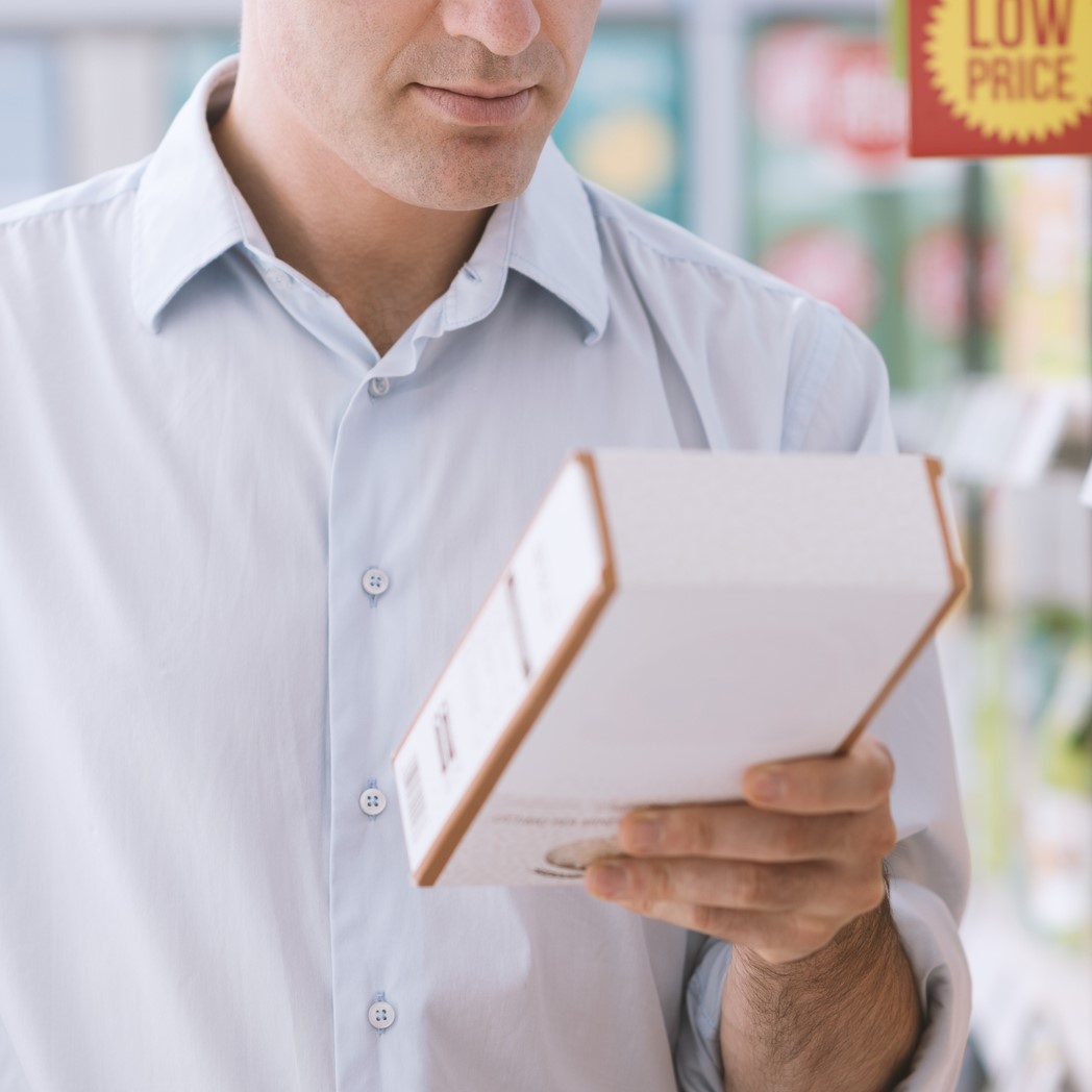 Man doing grocery shopping at the supermarket and reading a food label on a box.