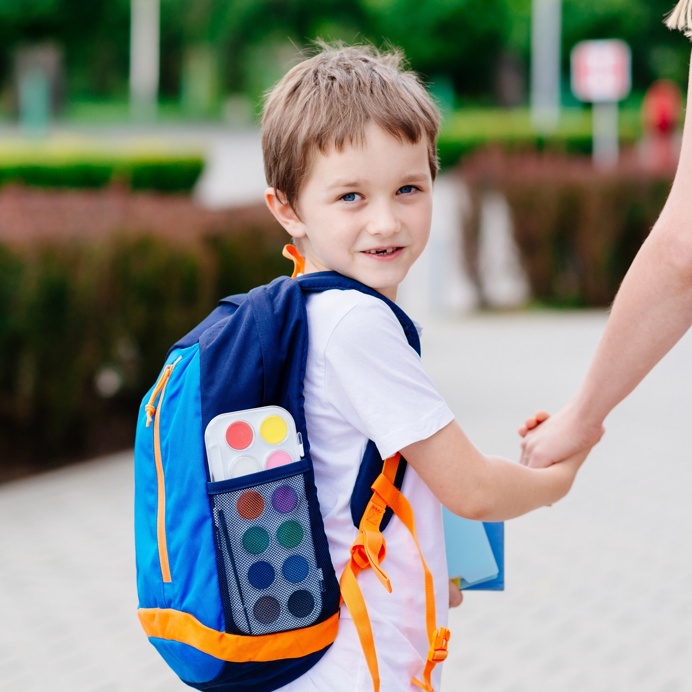 7-year-old boy with a backpack, holding his mother's hand in front of his school