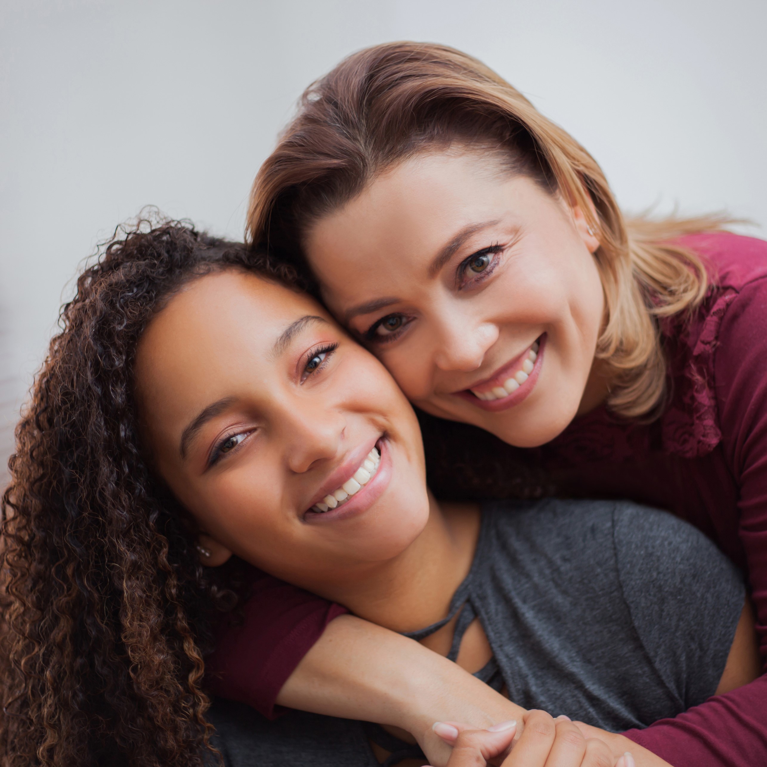 Portrait of a woman hugging her daughter, both people holding hands looking and smiling at the camera with a candid attitude